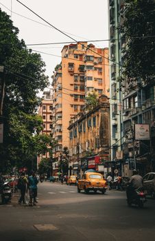 Vibrant street scene in Kolkata with iconic yellow taxi amid bustling city life and architecture.