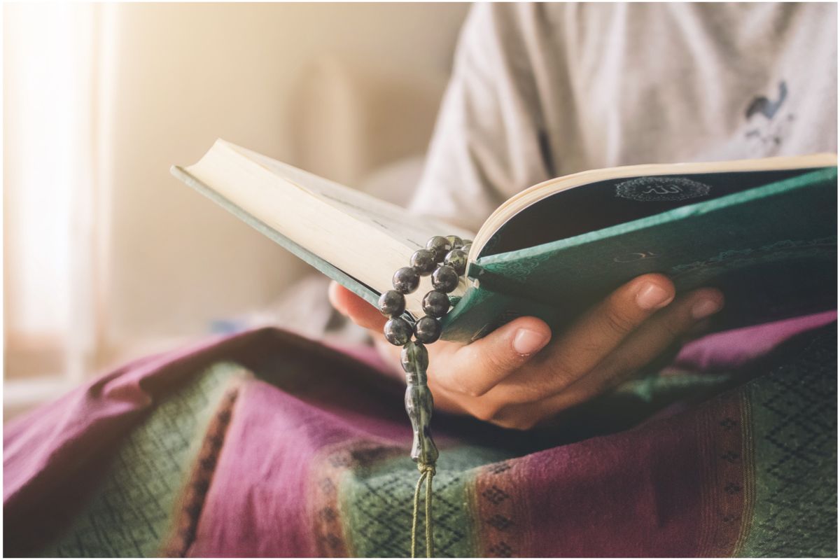 Hands raised in supplication beside a Quran, the aqiqah doa for a newborn