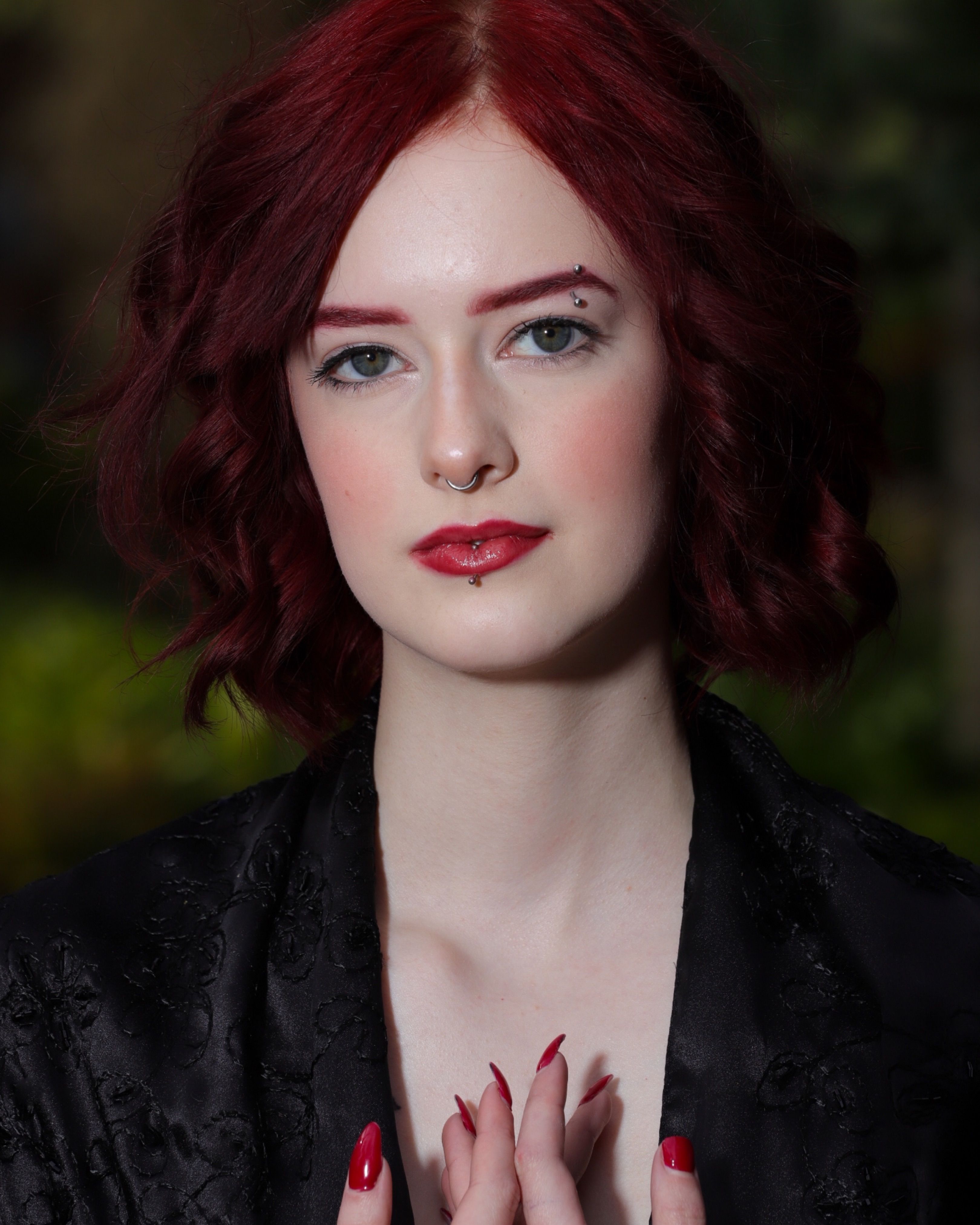 Elegant portrait of a woman with red hair and facial piercings in a classic setting.