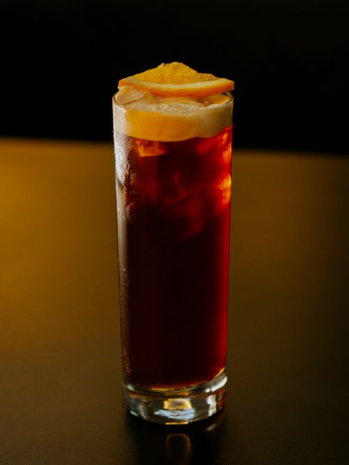 Free Tall glass of iced coffee with orange garnish against a dark background. Stock Photo