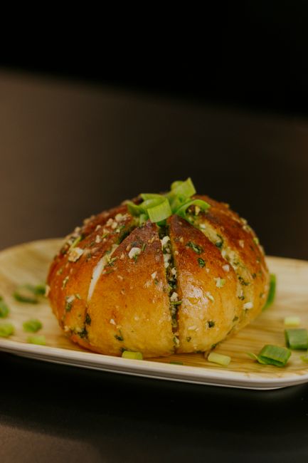 Sliced French bread with a golden, garlic-flecked crust and melted spread pooling in the toasted grooves, arranged on a wooden board.