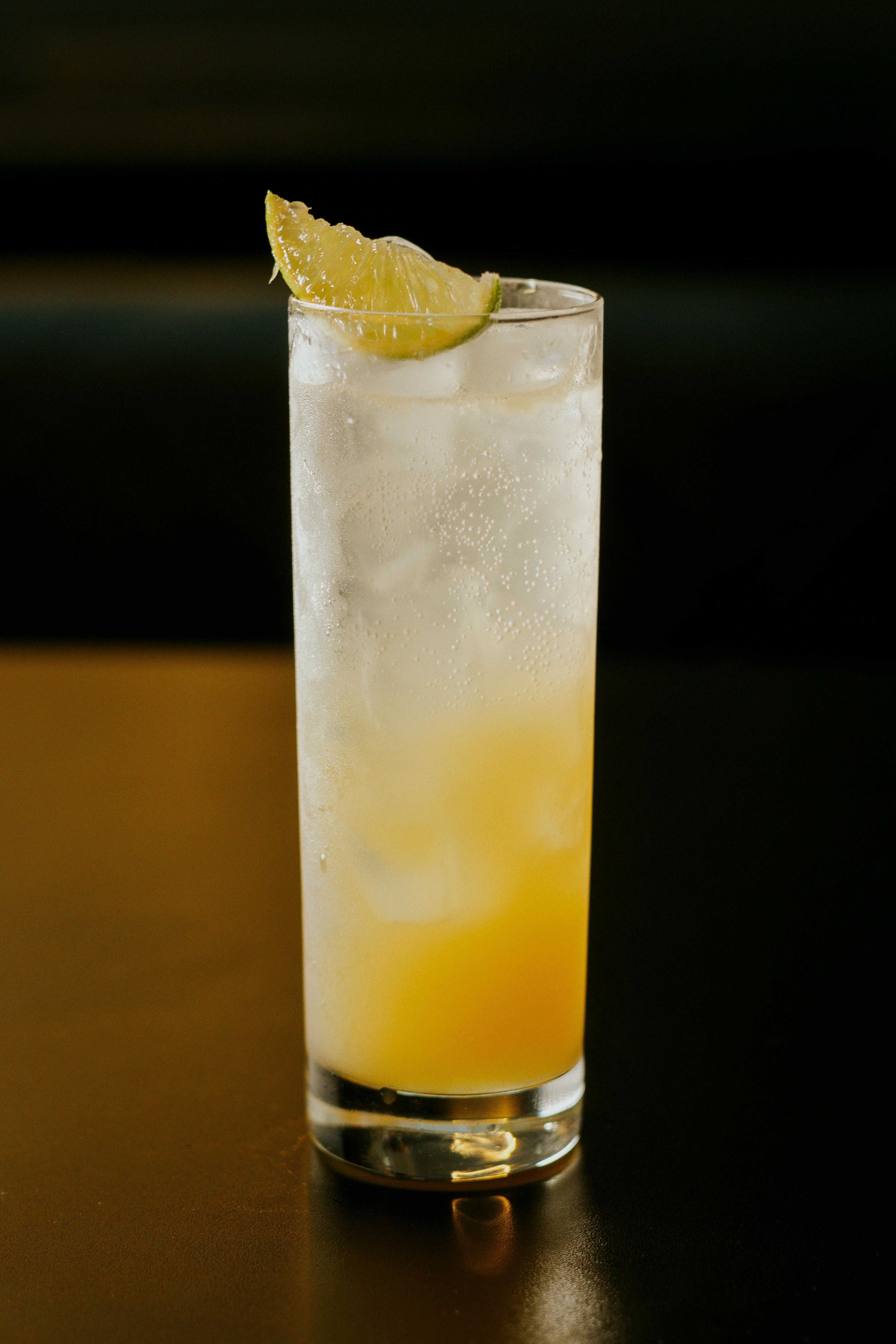 Tall glass of citrus cocktail with ice and lime wedge garnish, ideal for summer refreshments.