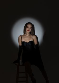 Studio portrait of a woman in an elegant black dress seated with dramatic lighting.