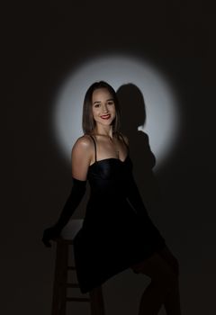 Studio portrait of a woman in a black dress, spotlight creates dramatic shadow.