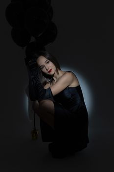 Woman in black dress holding black balloons in a studio shoot with dramatic lighting.