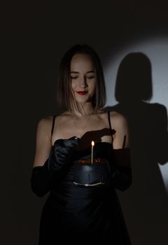 A glamorous woman in a black dress holds a black cake with a candle, creating a mysterious and elegant ambiance.