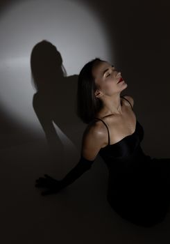 A stylish woman in a black dress posing elegantly with dramatic shadow play in a studio setting.