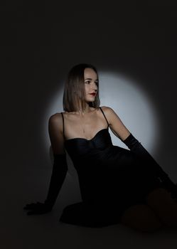 Chic portrait of a woman in a black dress with evening gloves, posing in a dramatic spotlight.
