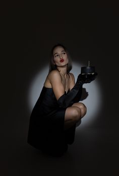 Glamorous woman in a dark studio setting, dressed in black, holding a decorative candle.