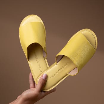 Close-up of yellow leather flip flops held against a neutral background, perfect for fashion and footwear themes.