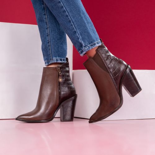 Free Close-up of chic brown leather ankle boots with high heels paired with denim jeans on a vibrant backdrop. Stock Photo