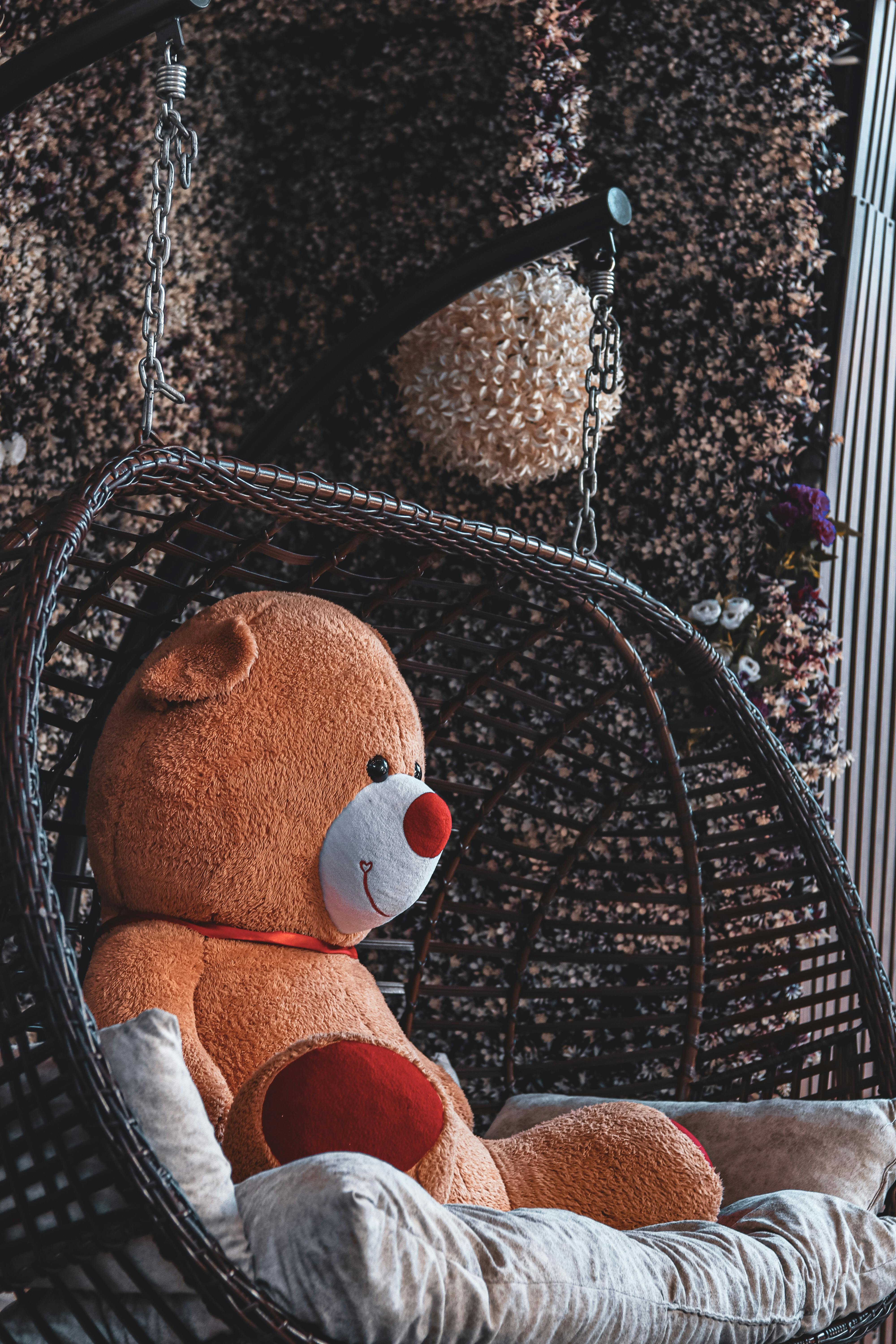 Free A charming teddy bear seated in a wicker chair, adding a cozy touch to a decorated indoor space. Stock Photo