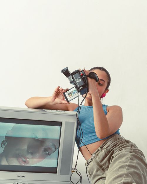 Free Woman filming with vintage camera next to CRT television screen indoors. Stock Photo