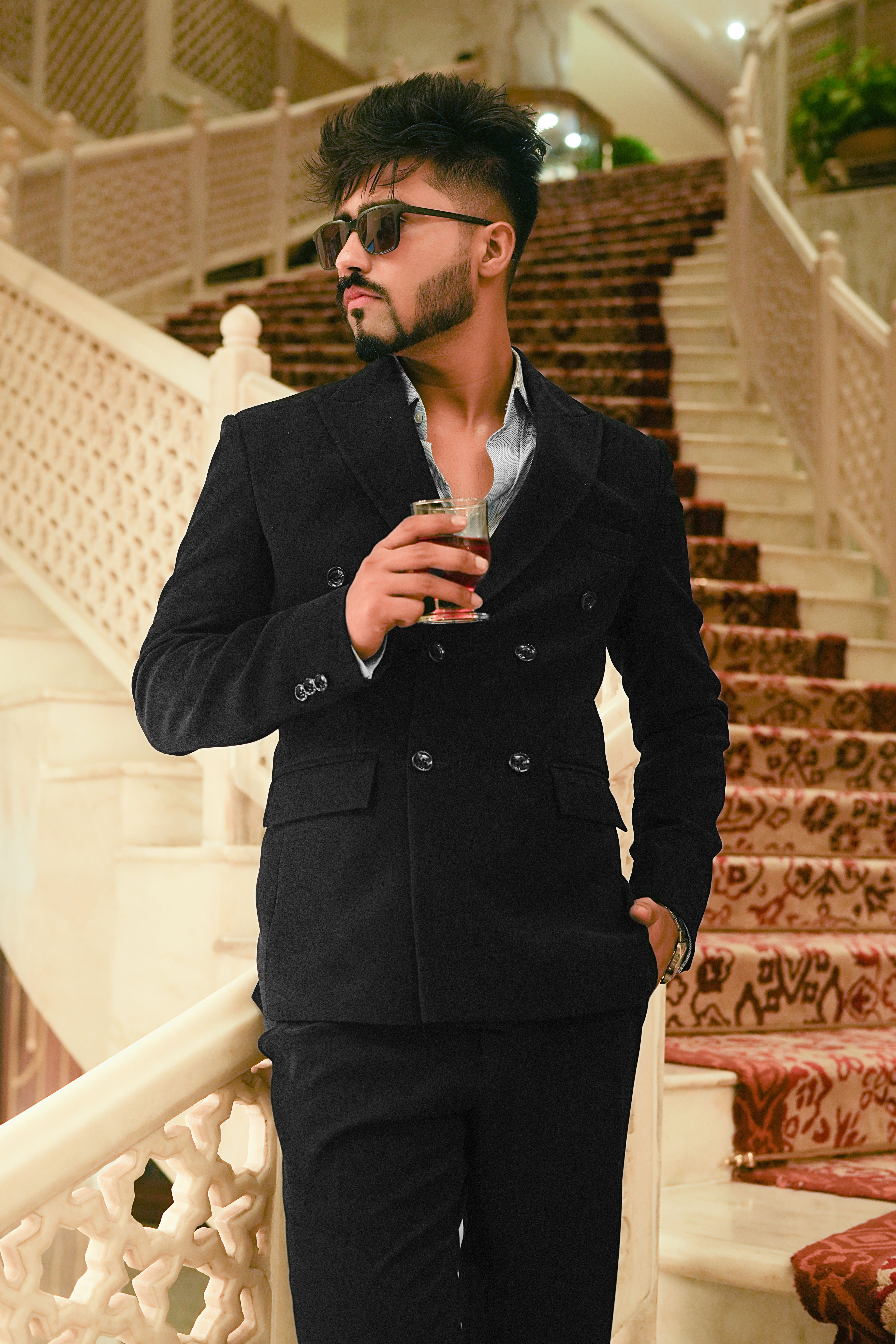 Elegant man in formal wear holding a drink on a luxurious staircase indoors.