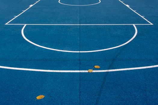 An empty blue basketball court with white lines and leaves on the surface.