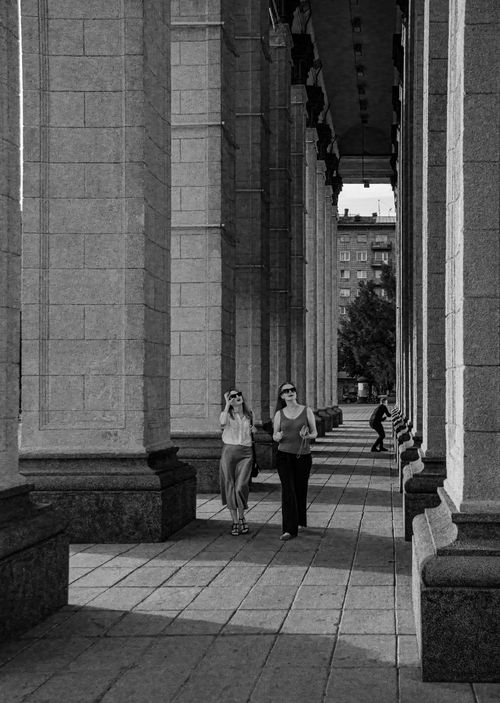 Free Two women walking among large columns, evoking a sense of historic architecture and daily life. Stock Photo