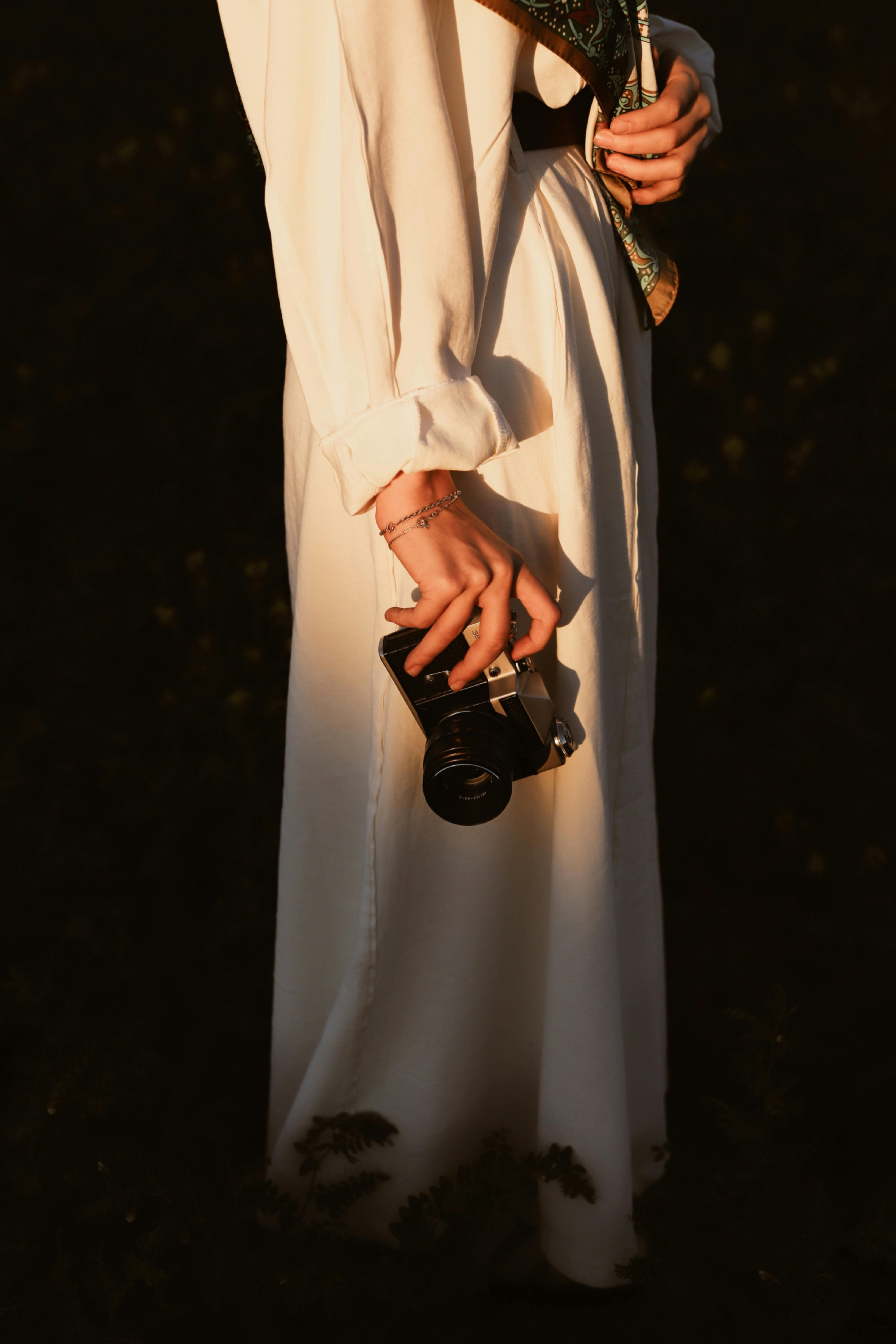 A woman in a flowing dress elegantly holds a vintage camera, capturing the essence of nostalgia.