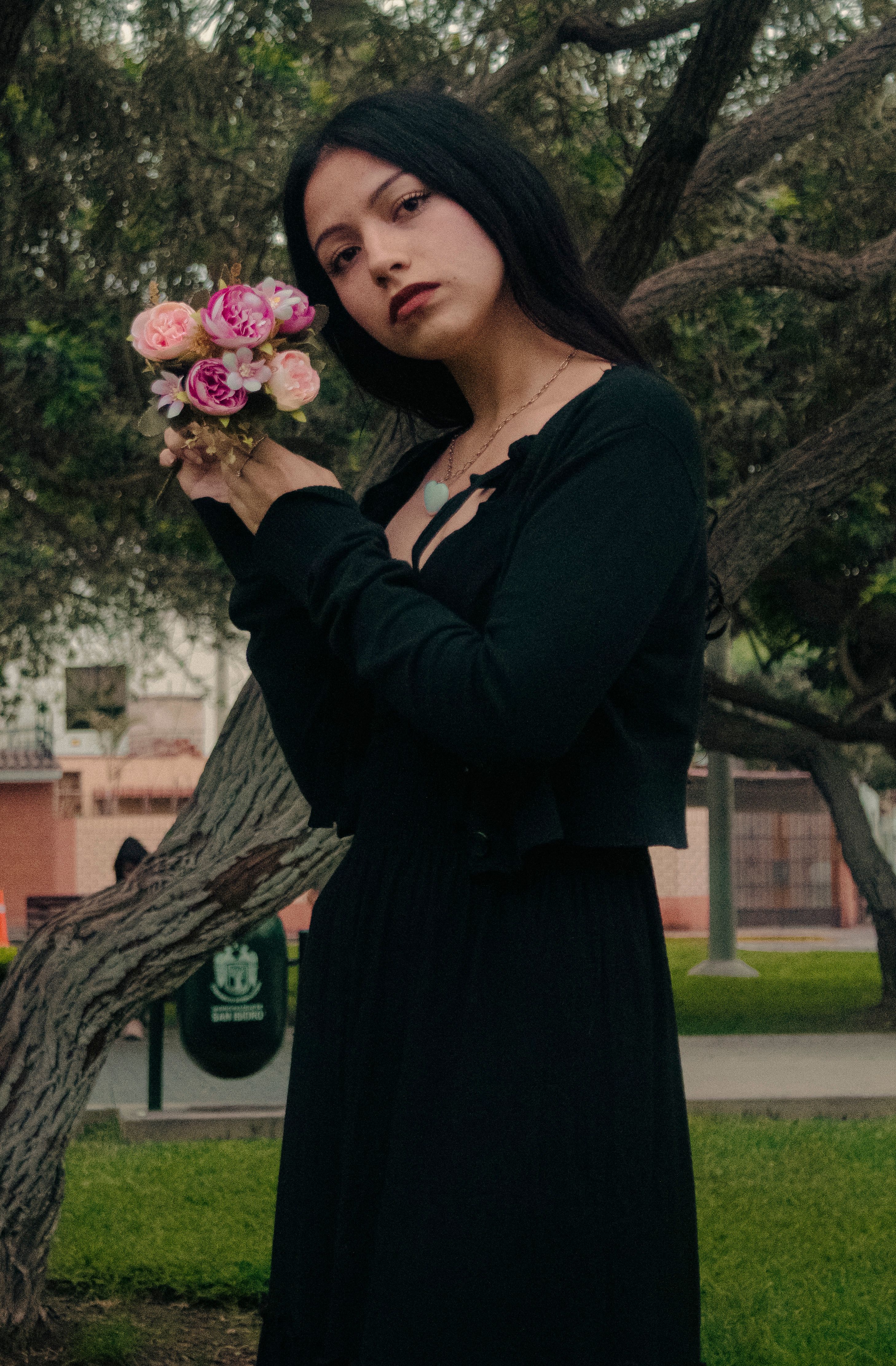 A woman in a dark dress holding a bouquet of flowers in a park setting, showcasing elegance and serene beauty.