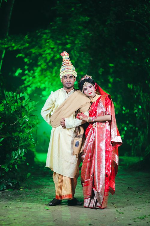 Free Couple in traditional Indian wedding attire posing outdoors with lush green backdrop. Stock Photo