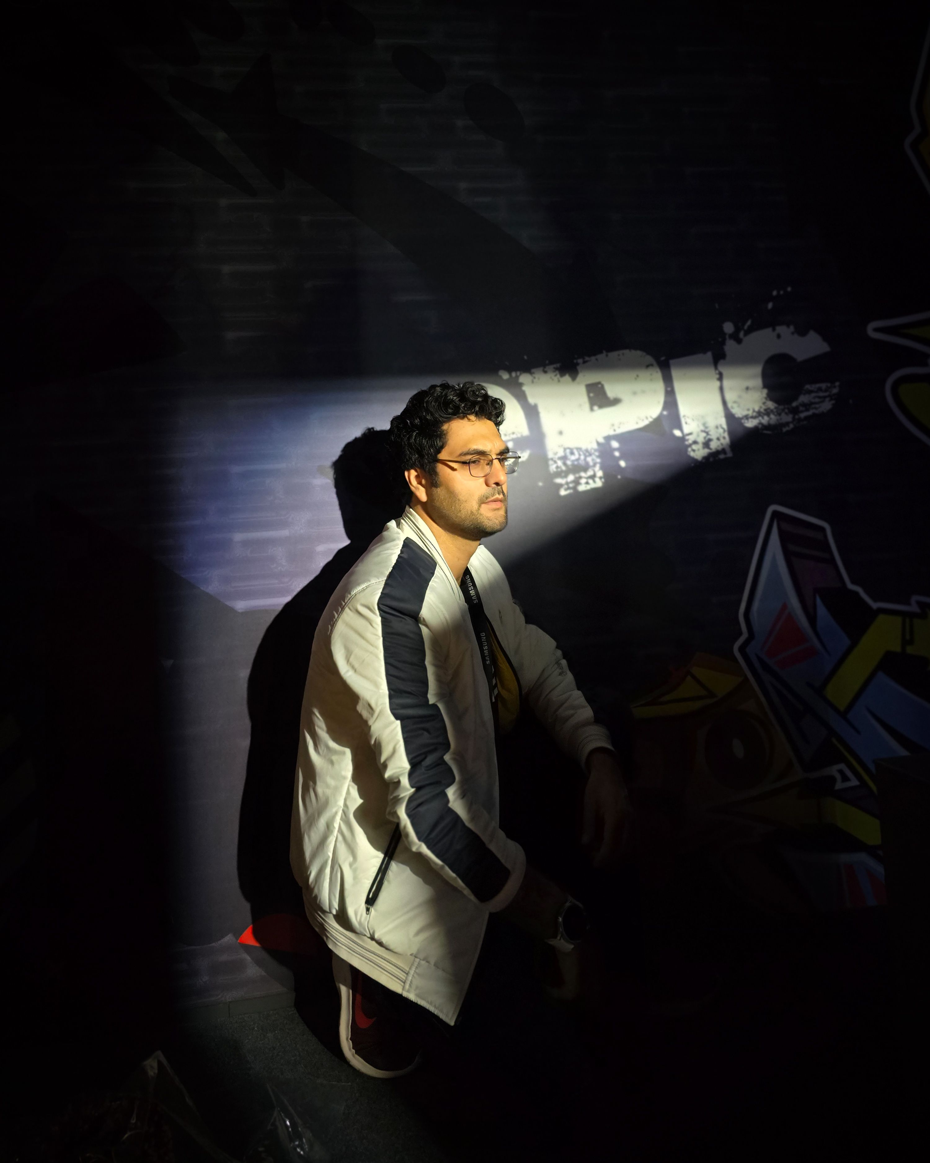 Artistic portrait of a man in a spotlight, highlighting moody atmosphere with graffiti background.