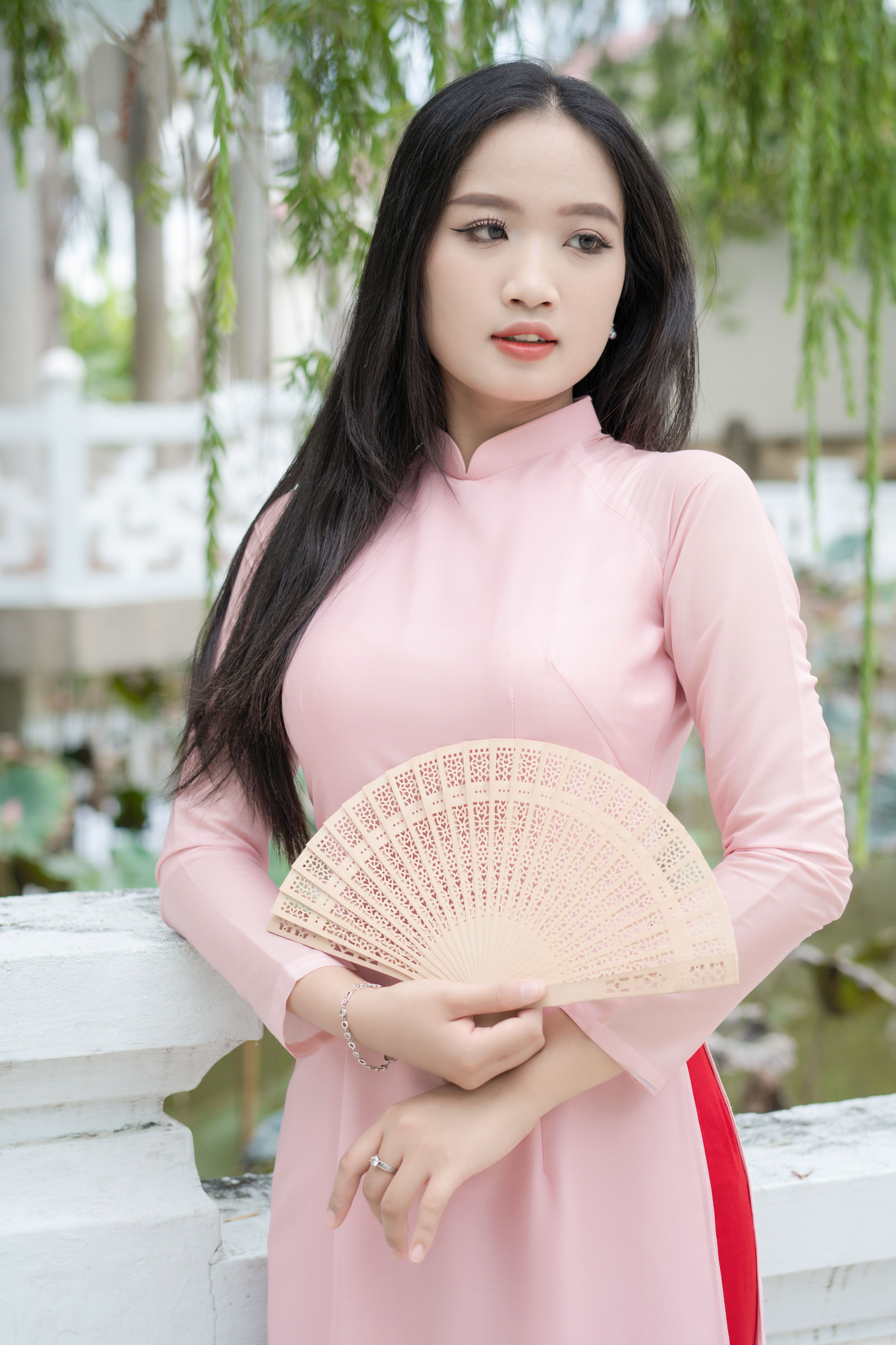 Young woman in traditional Ao Dai holding a fan in a serene garden.