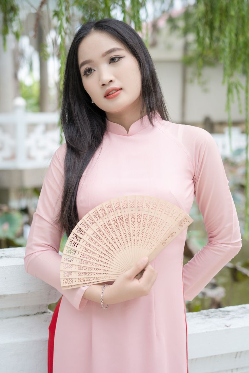 Vietnamese woman poses with hand fan in a garden wearing traditional Ao Dai.
