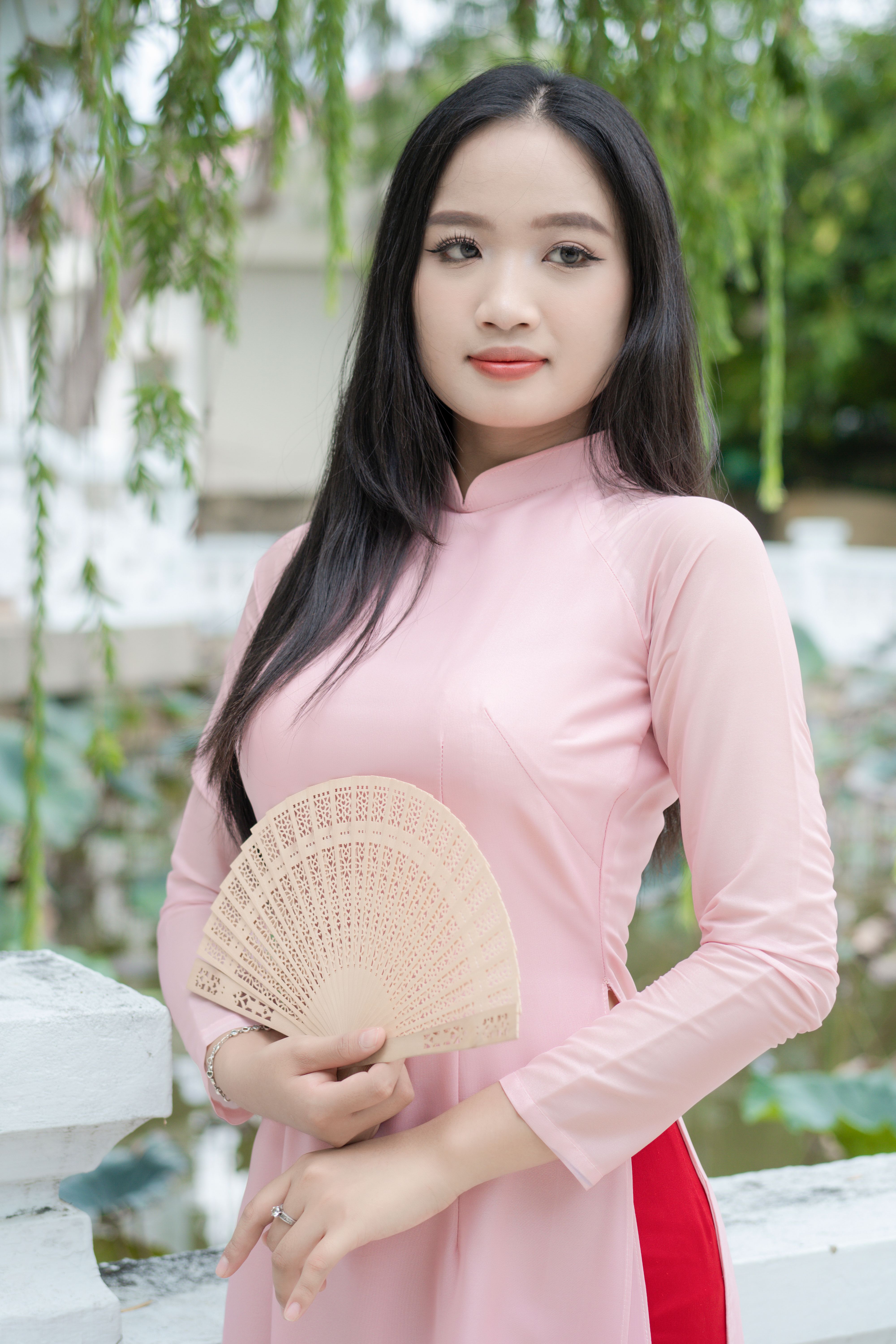 Asian woman in pink ao dai holding a hand fan, showcasing traditional fashion and elegance.