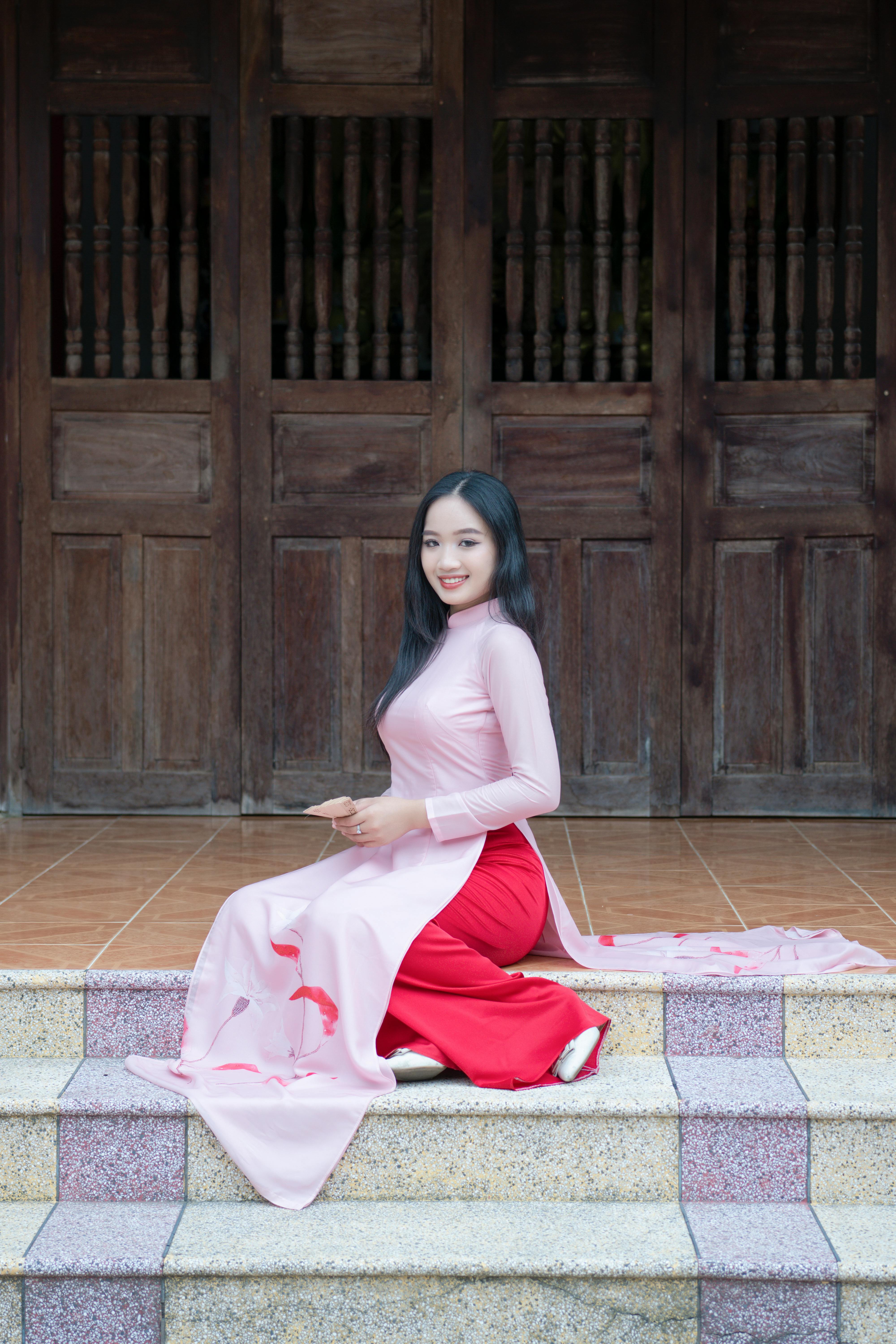 Smiling woman in traditional ao dai sitting on steps, exuding elegance.