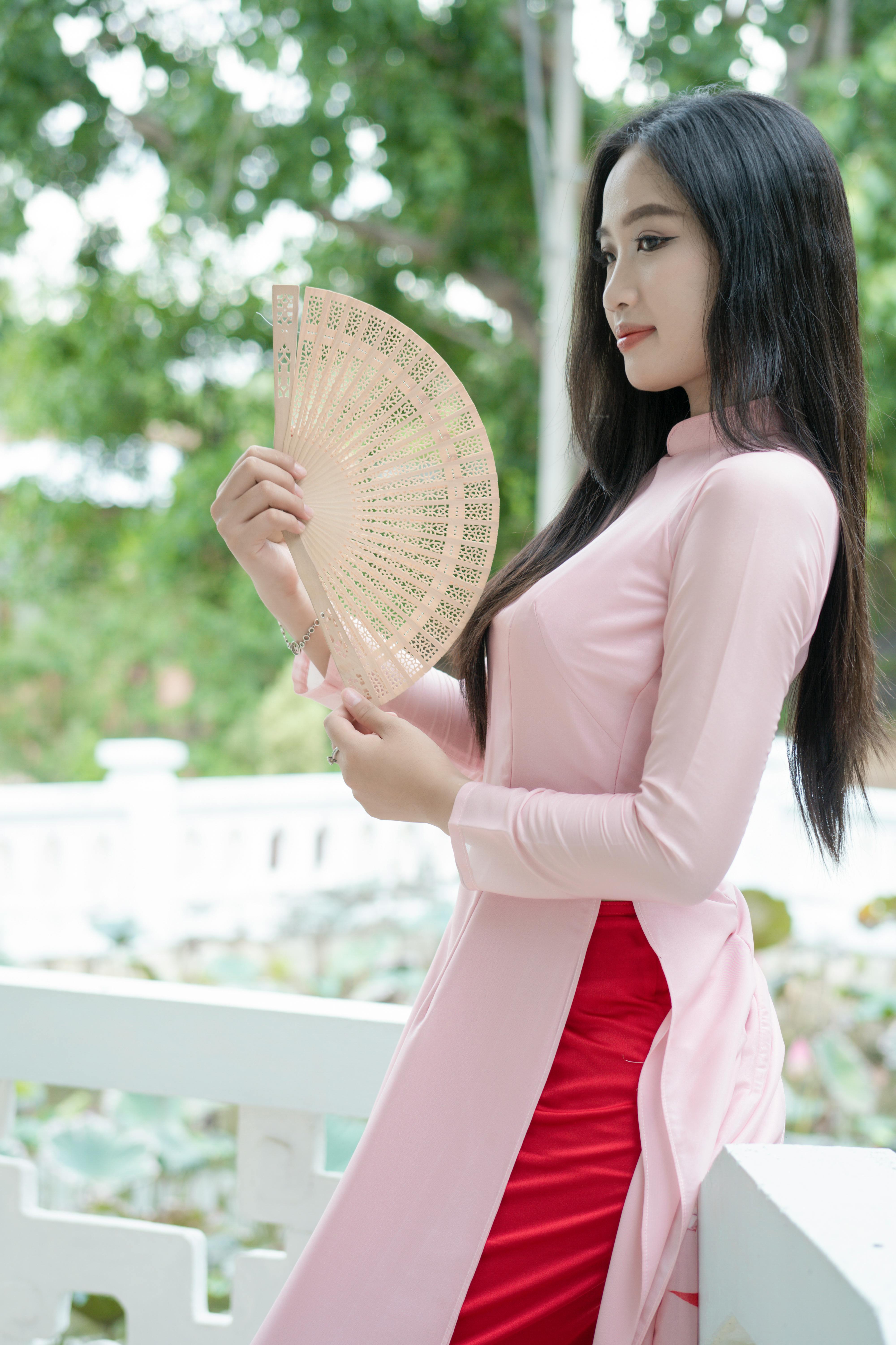 Brunette woman in traditional ao dai holding a hand fan outdoors.