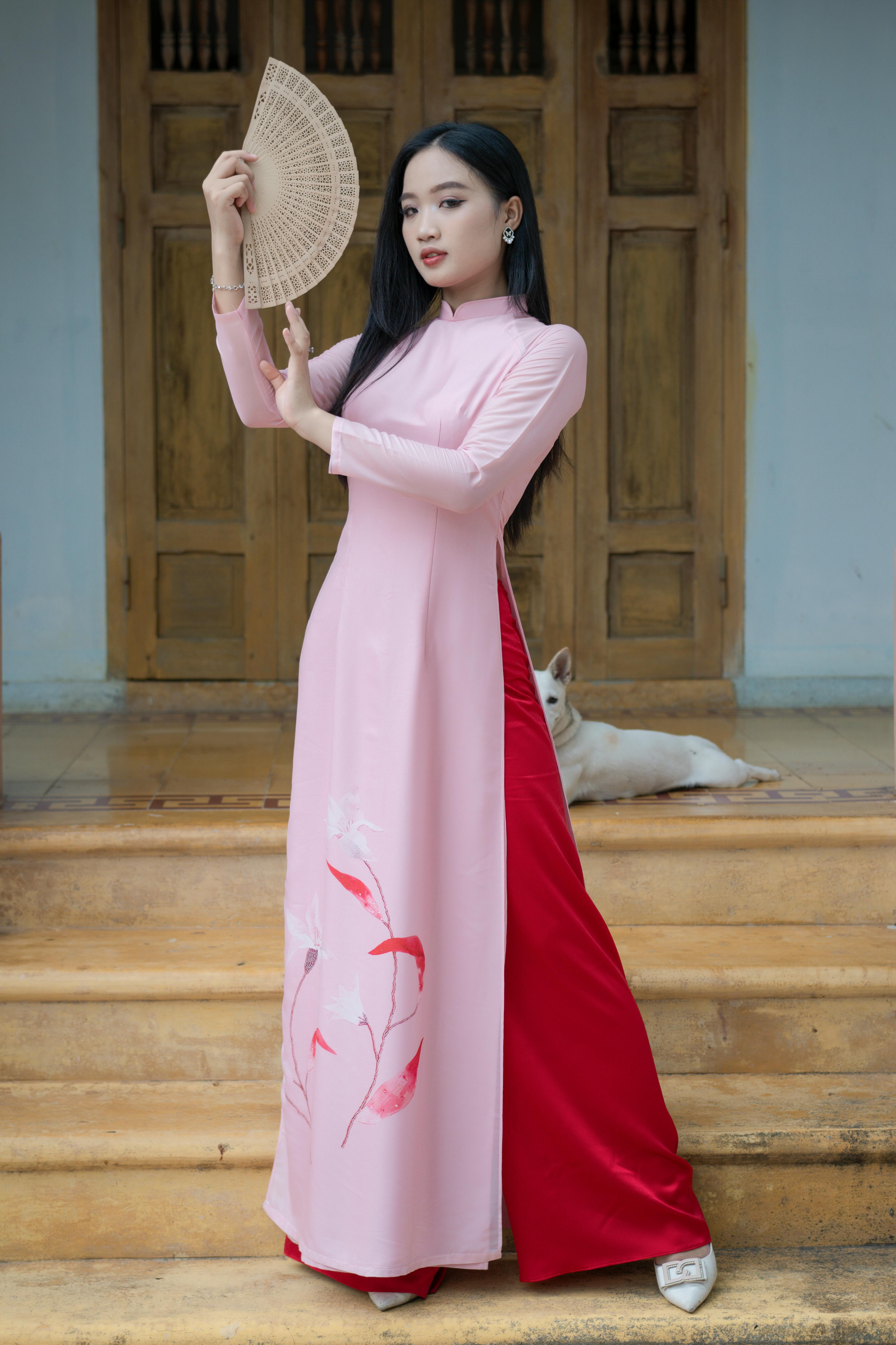 Free A woman poses gracefully in a traditional Vietnamese Ao Dai with a fan. Stock Photo