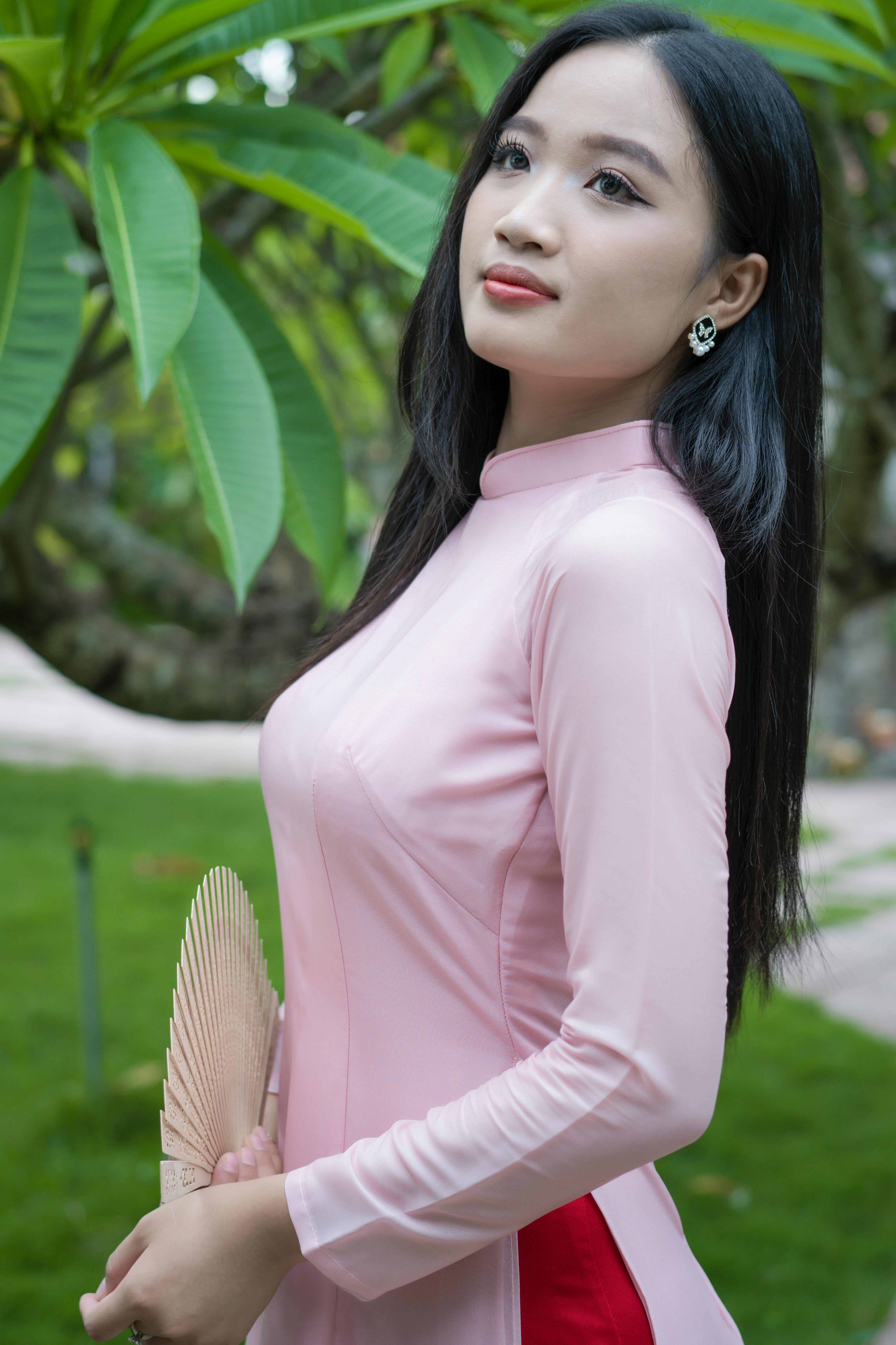 Elegant portrait of a young woman in a pink Ao Dai holding a fan outdoors.