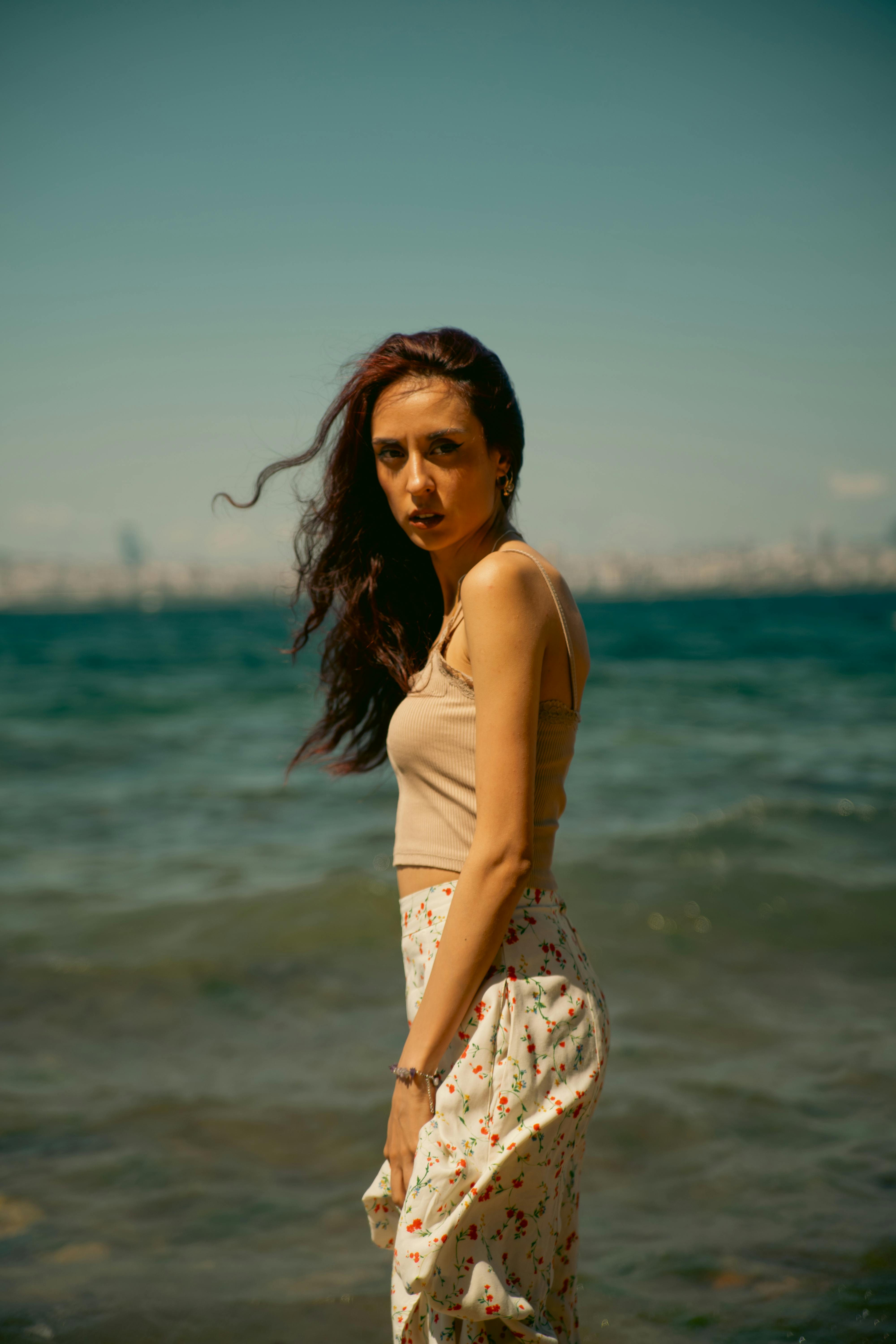 A stylish woman in a summer outfit stands by the seaside, soaking up the sun.