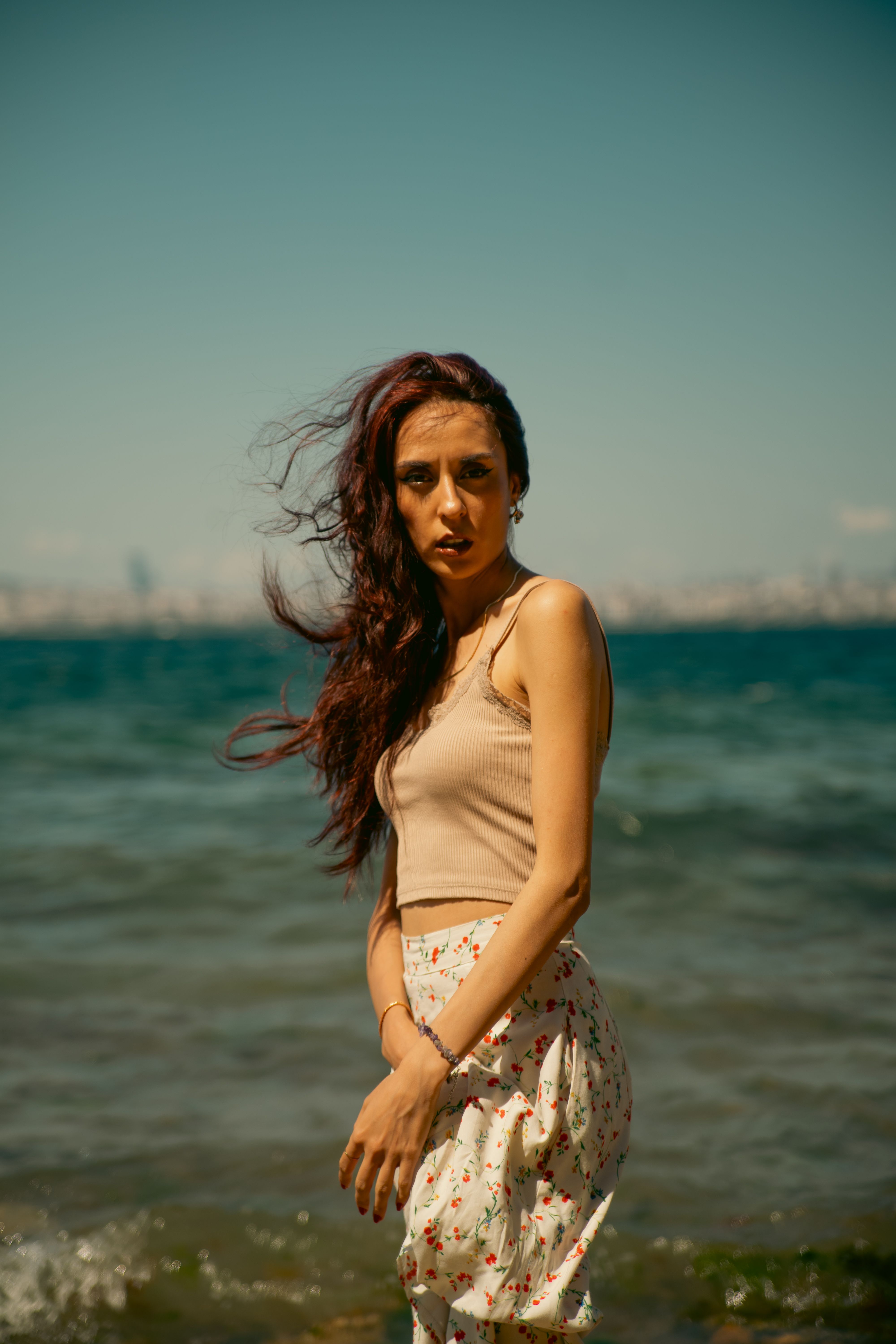 A red-haired woman in a white dress enjoys a bright summer day by the ocean.