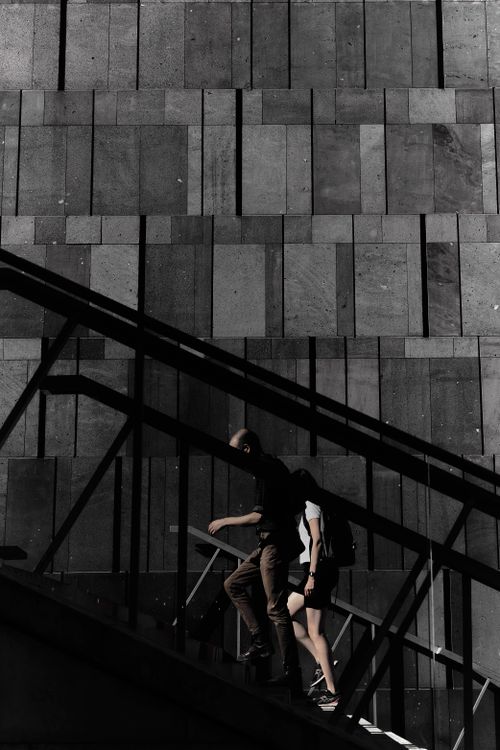 Free Silhouetted figures ascend urban stairs against a geometric concrete wall in Vienna, Austria. Stock Photo