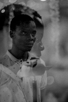 A contemplative black and white portrait of a man reflected in glass, creating a layered visual effect.