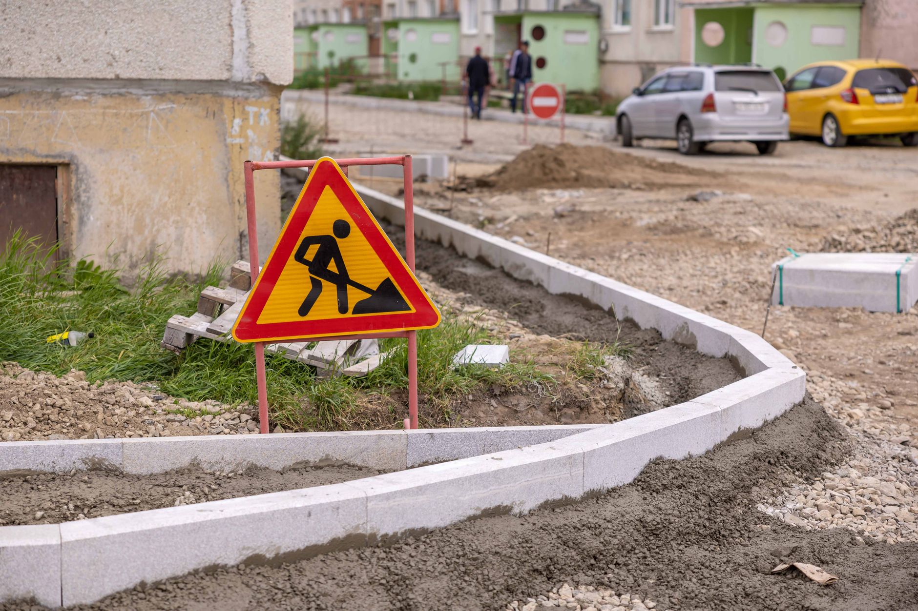 Urban road construction site with a caution sign and workers in the background.