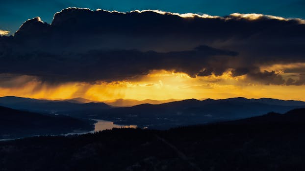 金色的色调在乌云笼罩的山地景观上投下，令人惊叹的日落