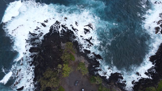 Photo by Jashith G Dramatic aerial shot of the rugged coastline in Maui, Hawaii, showcasing powerful ocean waves against dark rocks.