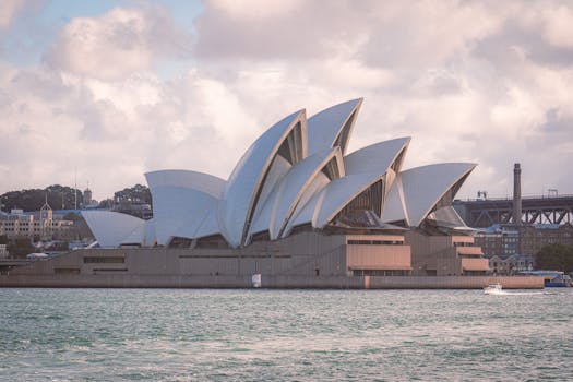 Iconic Sydney Opera House with a dramatic cloudy sky, showcasing modern architecture by the water.