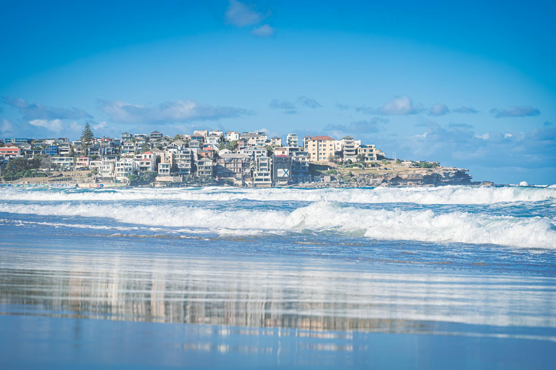 Vibrant Bondi Beach with waves lapping the shore and the urban skyline in the background under a bright blue sky.