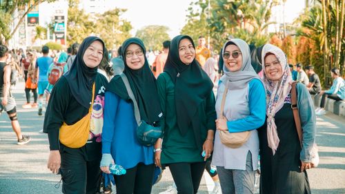Free Five women wearing hijabs smiling in an outdoor urban setting with a diverse crowd. Stock Photo