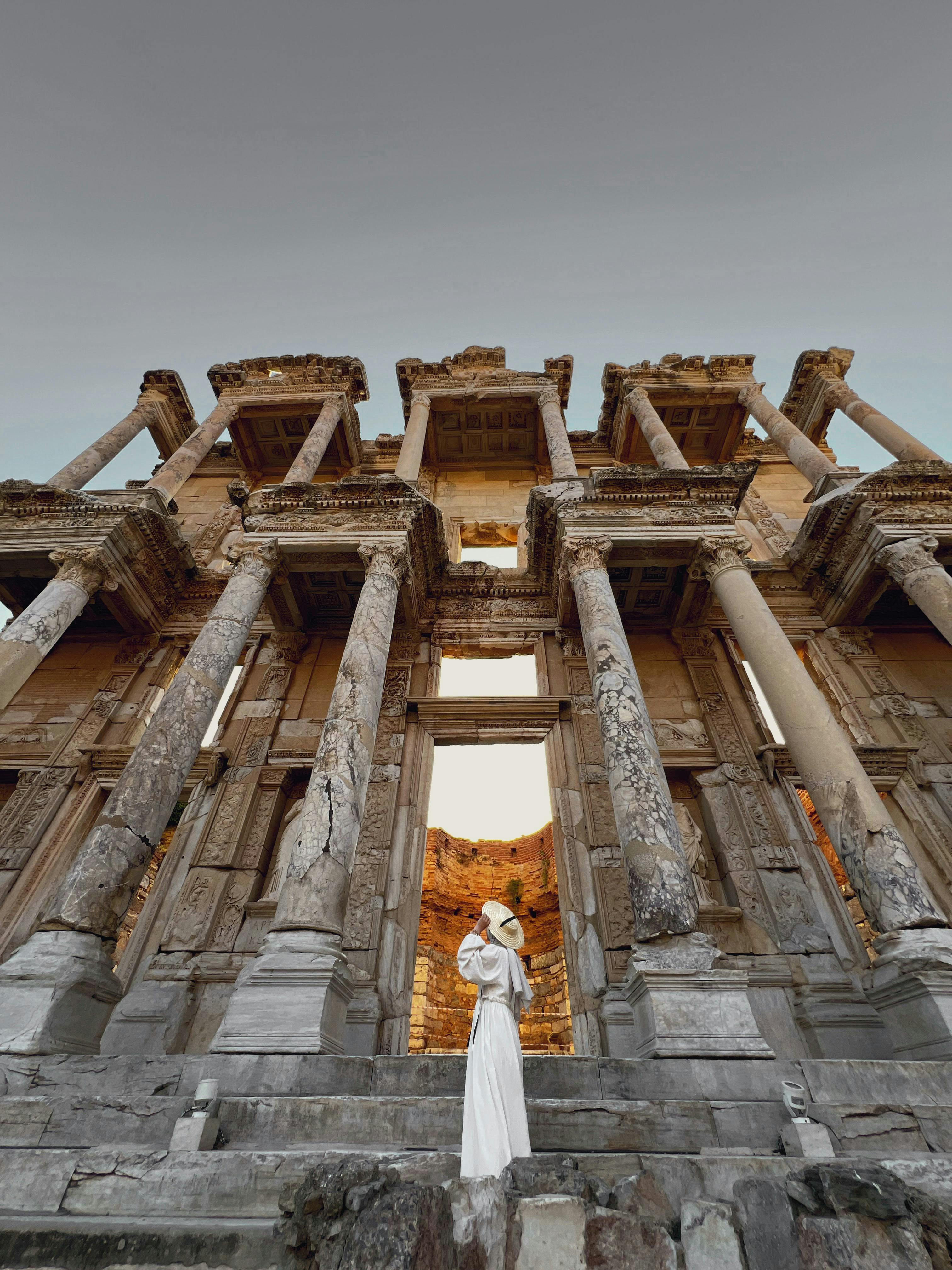 a woman in a white dress stands in front of the ancient ruins