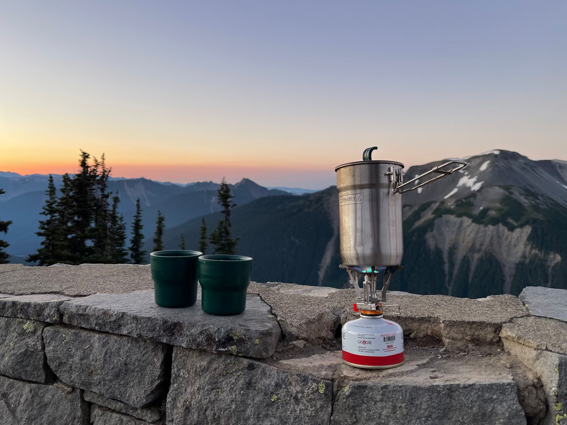 Outdoor morning scene with a camping stove set atop a mountain ridge at sunrise.