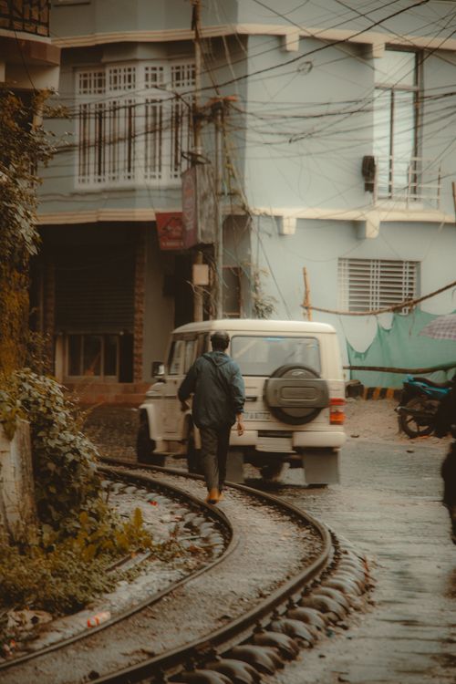 Free A person walks by train tracks and a car on a misty urban street, creating a moody scene. Stock Photo