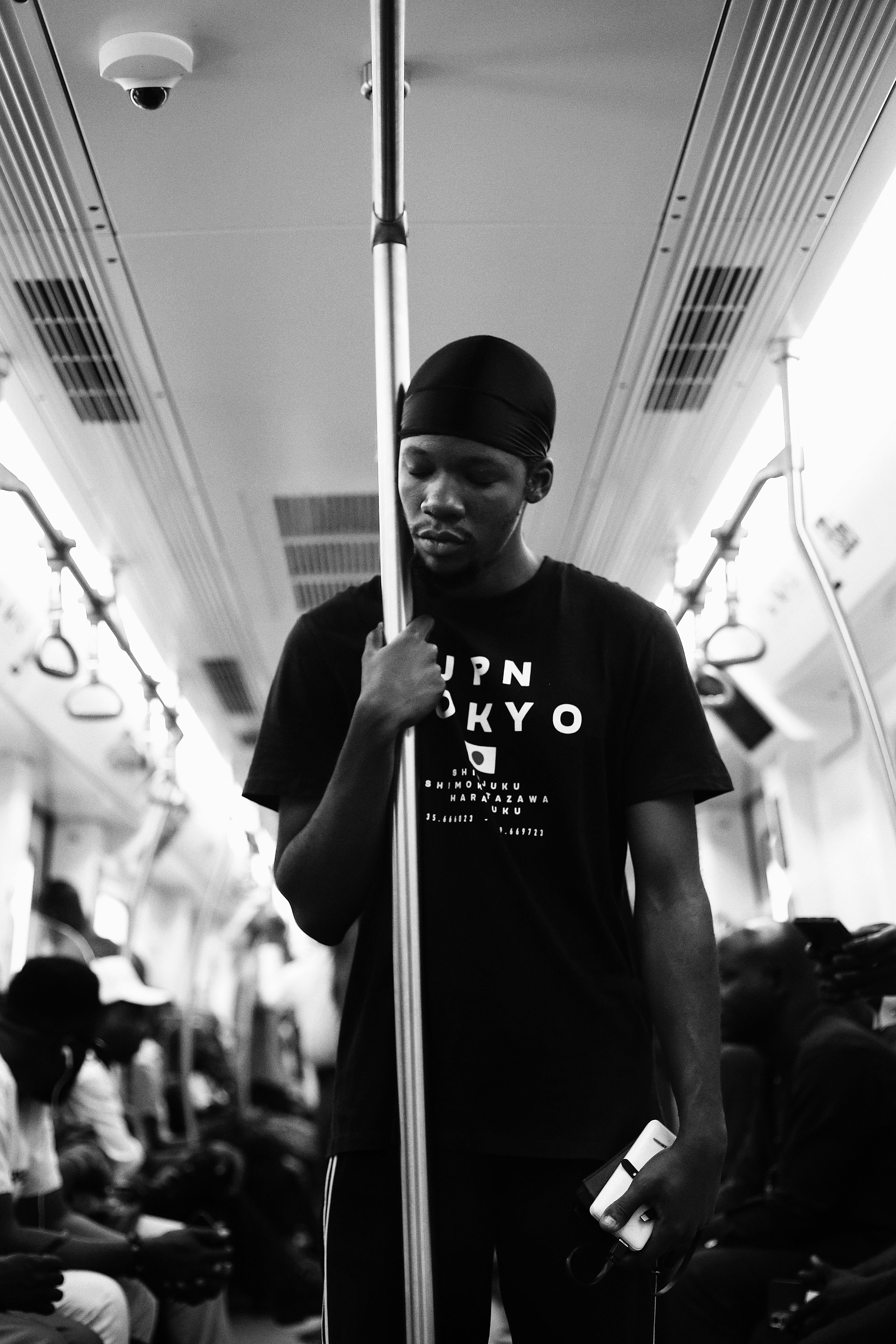 Black and white portrait of a man standing in a subway train holding a pole, with a distant expression.