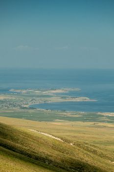 Expansive rural landscape meeting a tranquil sea under a clear summer sky.