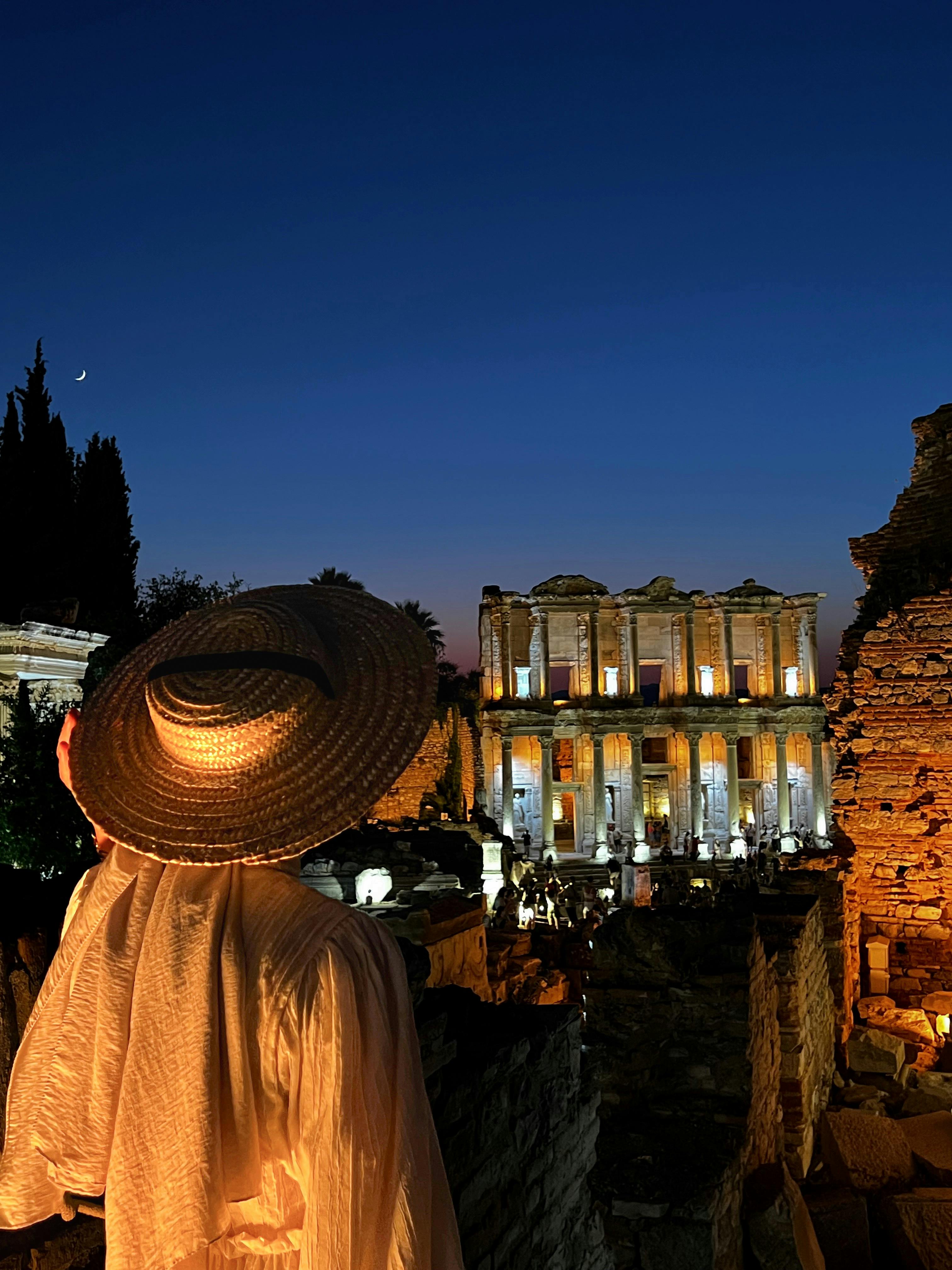 a woman in a hat stands in front of ruins