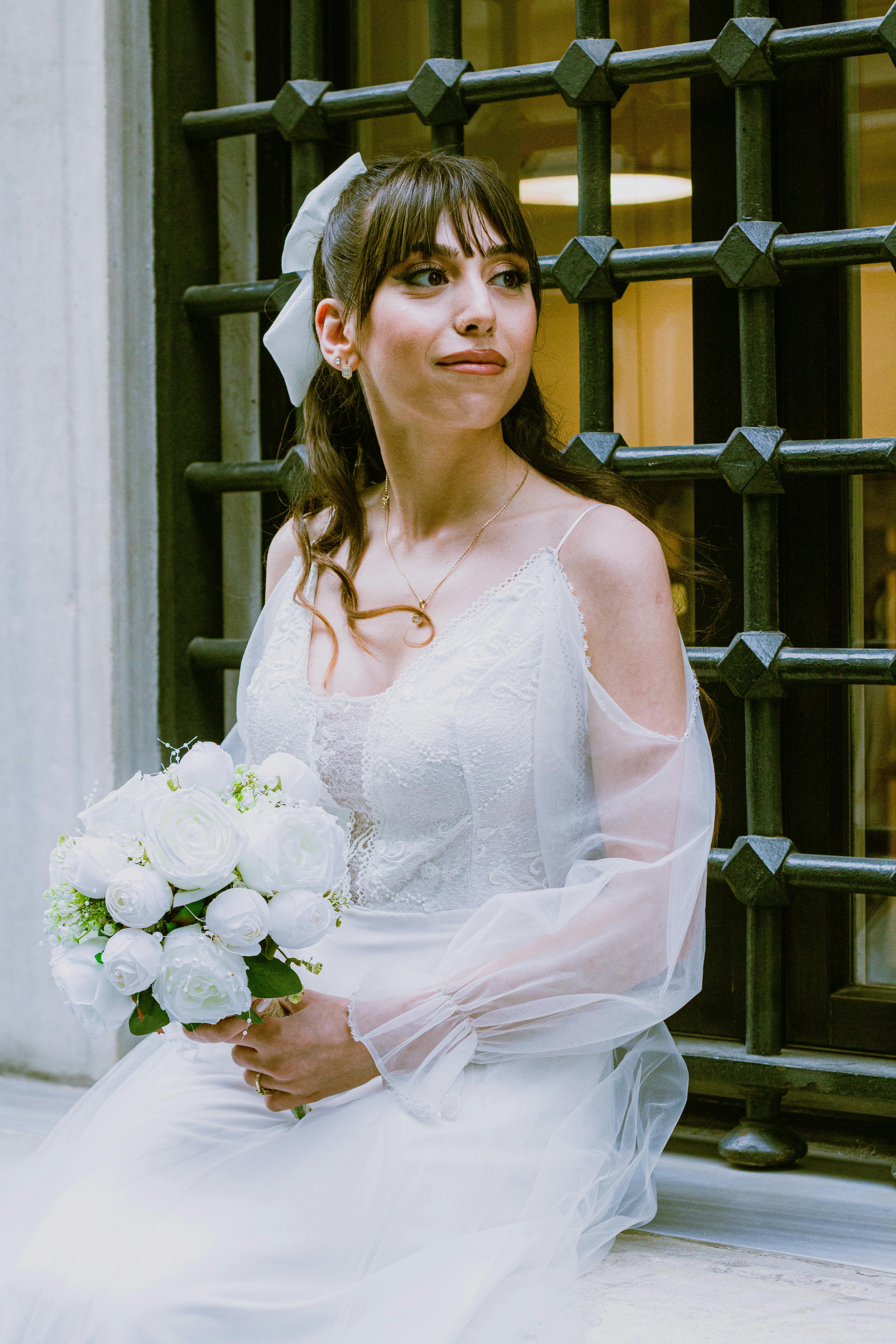 A bride in a white dress poses with a bouquet near a decorative window, embodying romantic elegance.