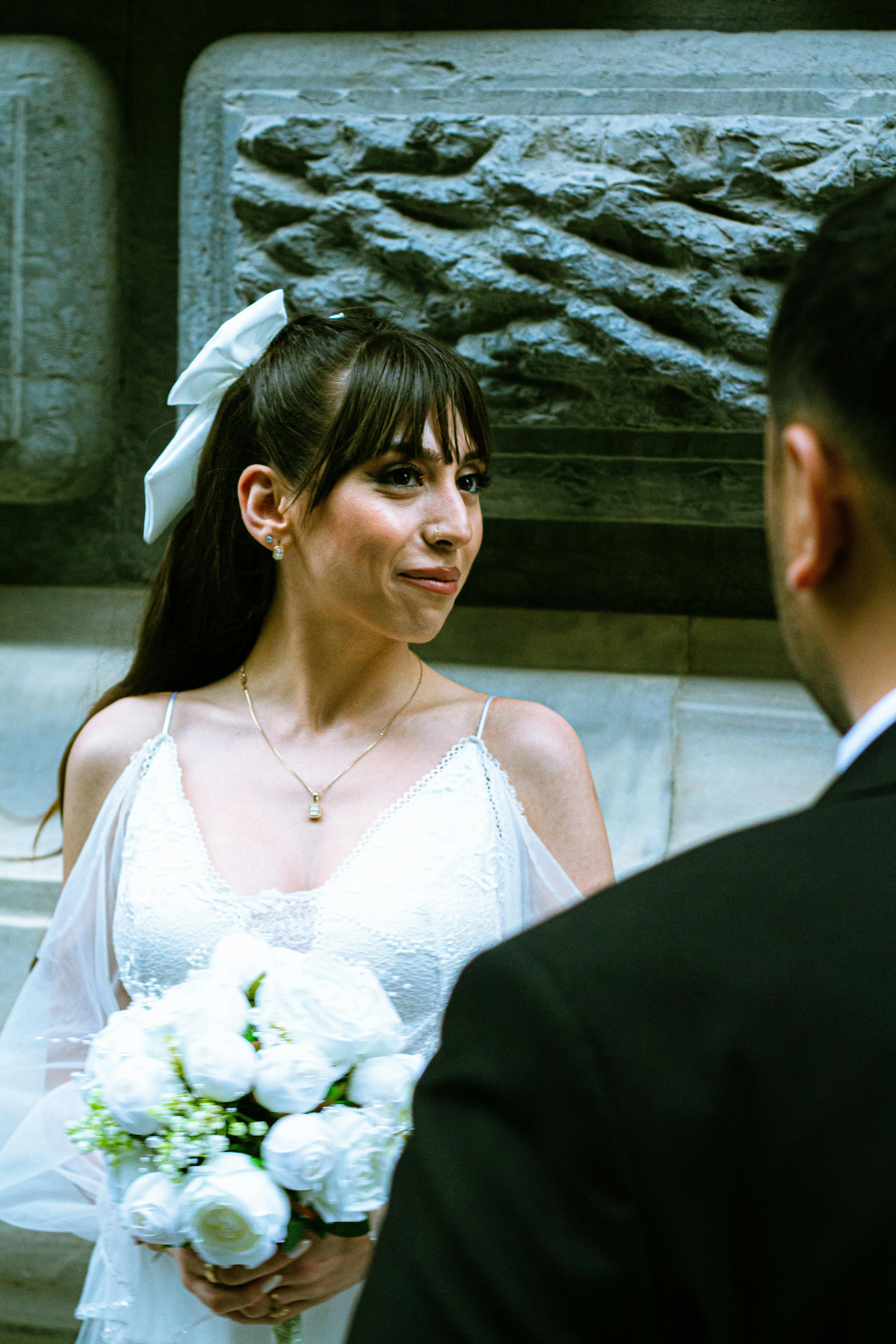 Bride holding a bouquet, standing outdoors during a wedding ceremony.