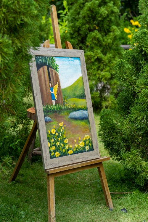 Free Painting on easel in a lush garden setting with vibrant greenery. Stock Photo